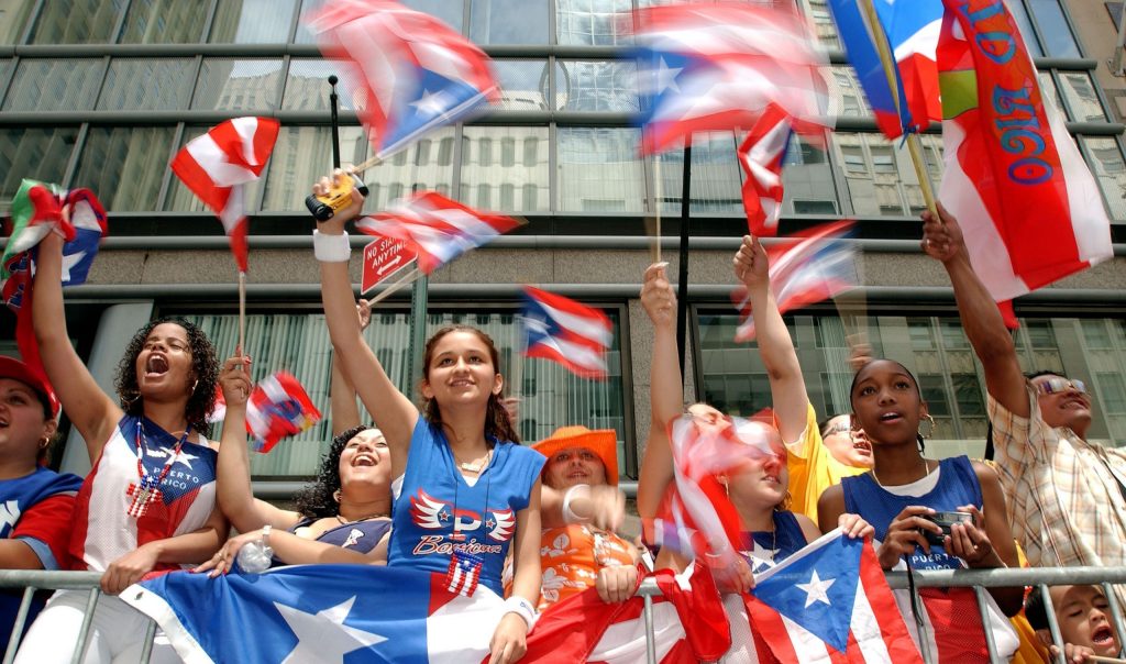 New York- June13: Parade goers cheer and wave Puerto Rican flags as they watch athe parade proceed up Fifth Avenue during the Ninth Annual Puerto Rican Day Parade June 13, 2004 in New York City. (Photo by Stephen Chernin/Getty Images)